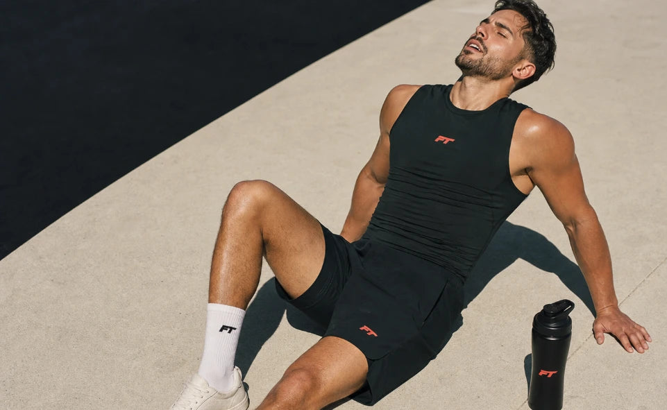 Tired man in black workout gear resting on concrete with a water bottle.